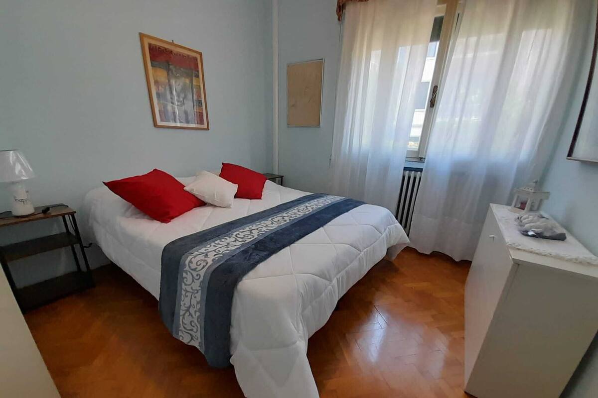 A bedroom with a bed, a nightstand, a radiator, and a small table with a lamp.