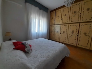 A bedroom with a bed, a window with curtains, a lamp, and a wardrobe with decorative panels. - House Seven Venice Beach (Venice)