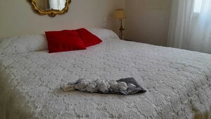 A neatly made bed with a white lace bedspread, two red pillows, and a folded towel on the bed.
