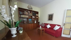 A living room with a red sofa, a wooden coffee table, a bookshelf, and a white vase with flowers.