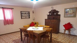 A dining area with a wooden table and chairs, a patterned floor, a cabinet, and a window with a checkered curtain.
