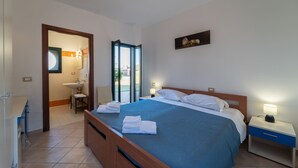 Ein Schlafzimmer mit Bett, Nachttisch und Blick durch eine offene Tür auf ein Badezimmer.