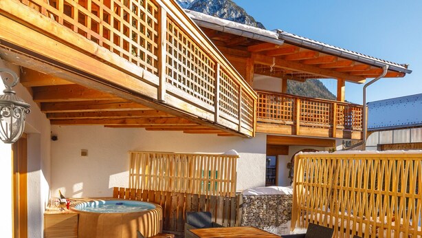 A wooden outdoor patio with a hot tub, seating area, and a view of mountains. - Alpenloft 1.0 (Mittenwald)