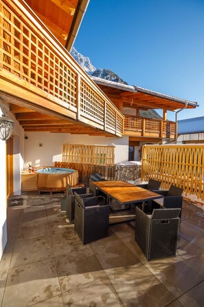 A wooden outdoor patio with a hot tub, seating area, and a view of mountains. - Alpenloft 1.0 (Mittenwald)