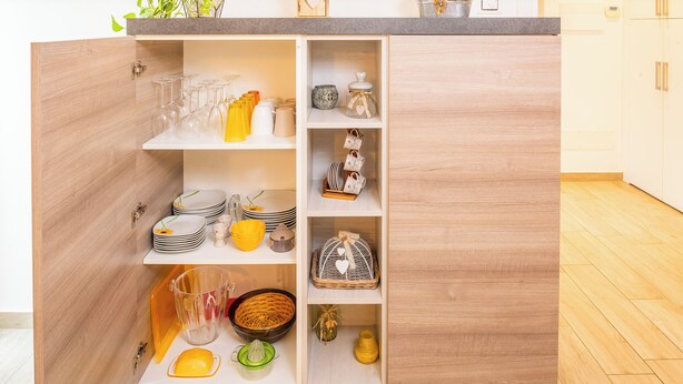 Een keuken met houten kastjes, planken met glazen en keukengerei.