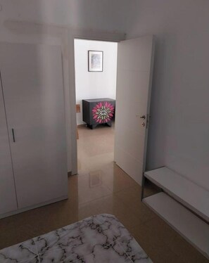 Una habitación con una cama, un armario, una mesita pequeña con un diseño llamativo y una puerta que da a otra estancia.