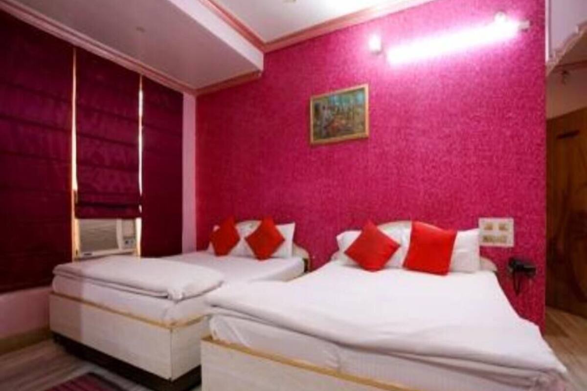 Una habitació d'hotel amb dos llits, cadascun amb roba de llit blanca i almoinos vermells. Les parets s ón de color rosa i hi ha un quadre penjat a la paret.