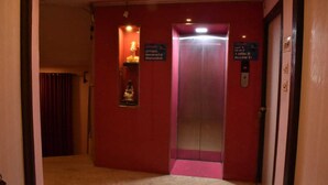 A hallway with a red wall, an elevator, and a small display case with a statue. - Hotel Shri Ram International (Varanasi)