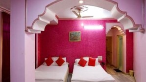 A room with two beds, a ceiling fan, and a pink wall. - Hotel Shri Ram International (Varanasi)