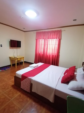 A hotel room with a bed, a desk, a TV, and a window with curtains. - OYO 879  Lauriens Budget Hotel 2 (Tagaytay)