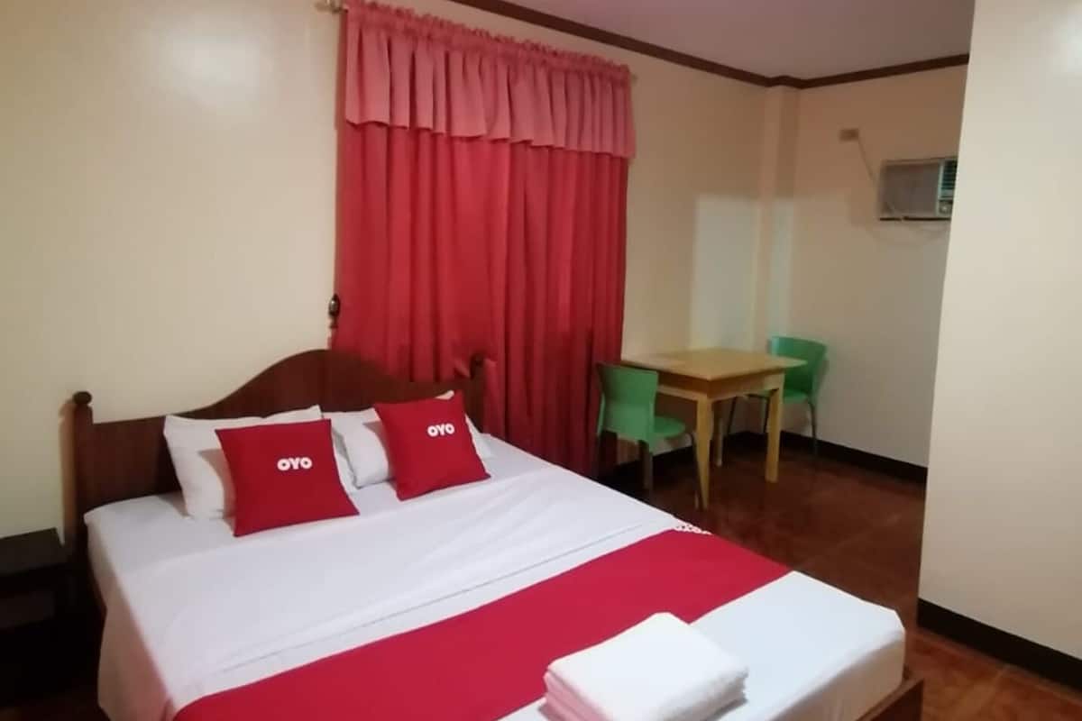 A hotel room with a wooden bed, red and white bedding, a desk, and a chair.