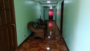 A hallway with patterned flooring, a wicker chair, a door, and a red curtain in the background. - OYO 879  Lauriens Budget Hotel 2 (Tagaytay)