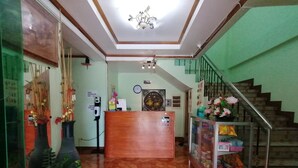 A reception area with a wooden reception desk, a clock, a hand sanitizer dispenser, and a staircase with a metal railing. - OYO 879  Lauriens Budget Hotel 2 (Tagaytay)