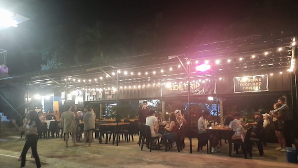 An outdoor dining area with tables and chairs, a stage with a sign, and a crowd of people. - OYO 879  Lauriens Budget Hotel 2 (Tagaytay)