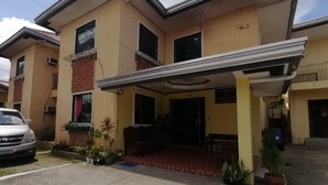 A two-story building with a covered entrance, potted plants, and a parked car. - OYO 879  Lauriens Budget Hotel 2 (Tagaytay)
