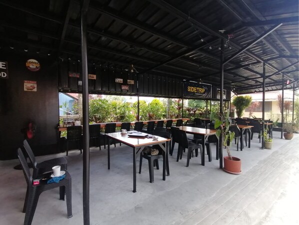 An outdoor cafe with tables and chairs, a sign reading "SIDETRIP", and potted plants.
