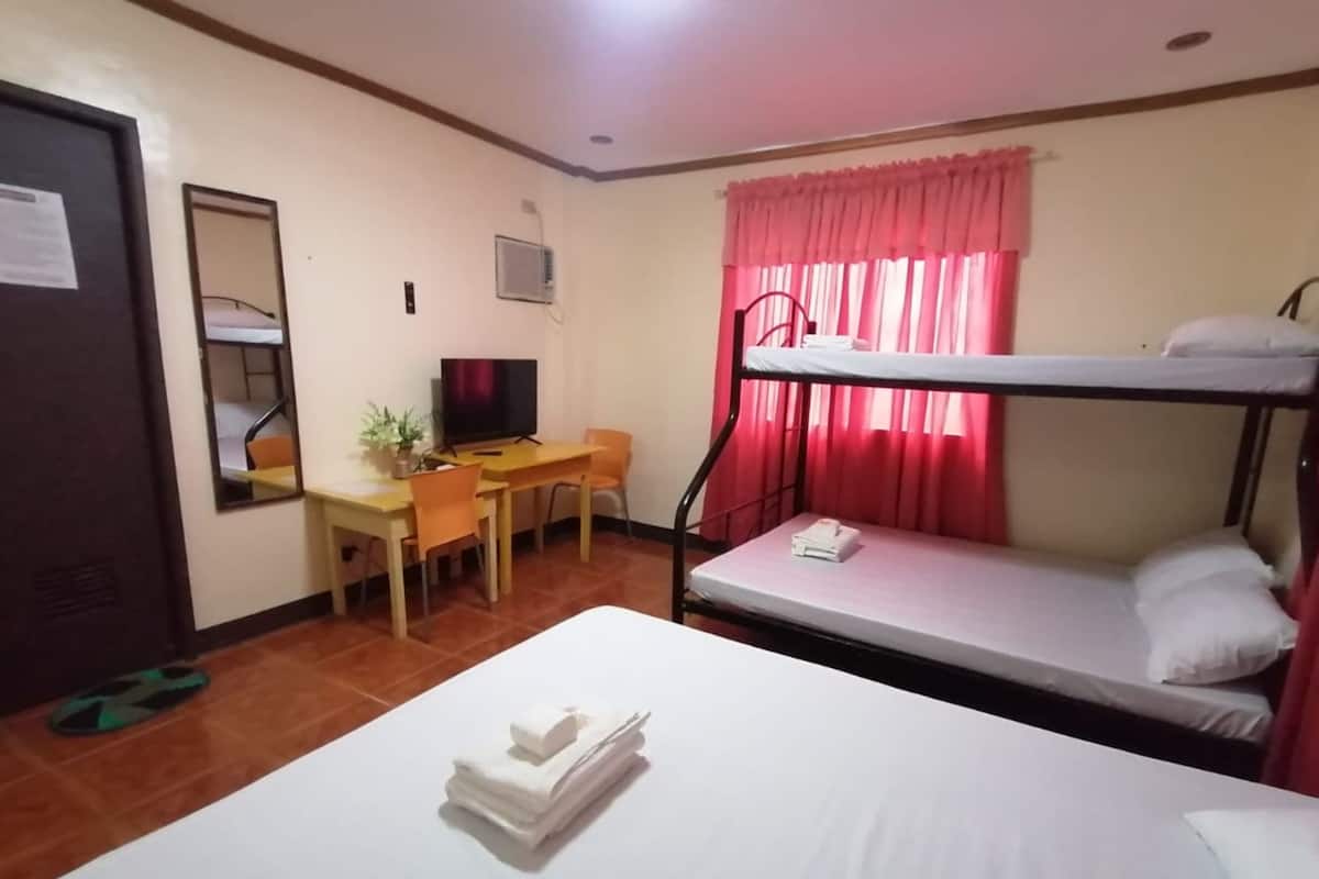 A hotel room with a bunk bed, a desk with a chair, a television, and a mirror.