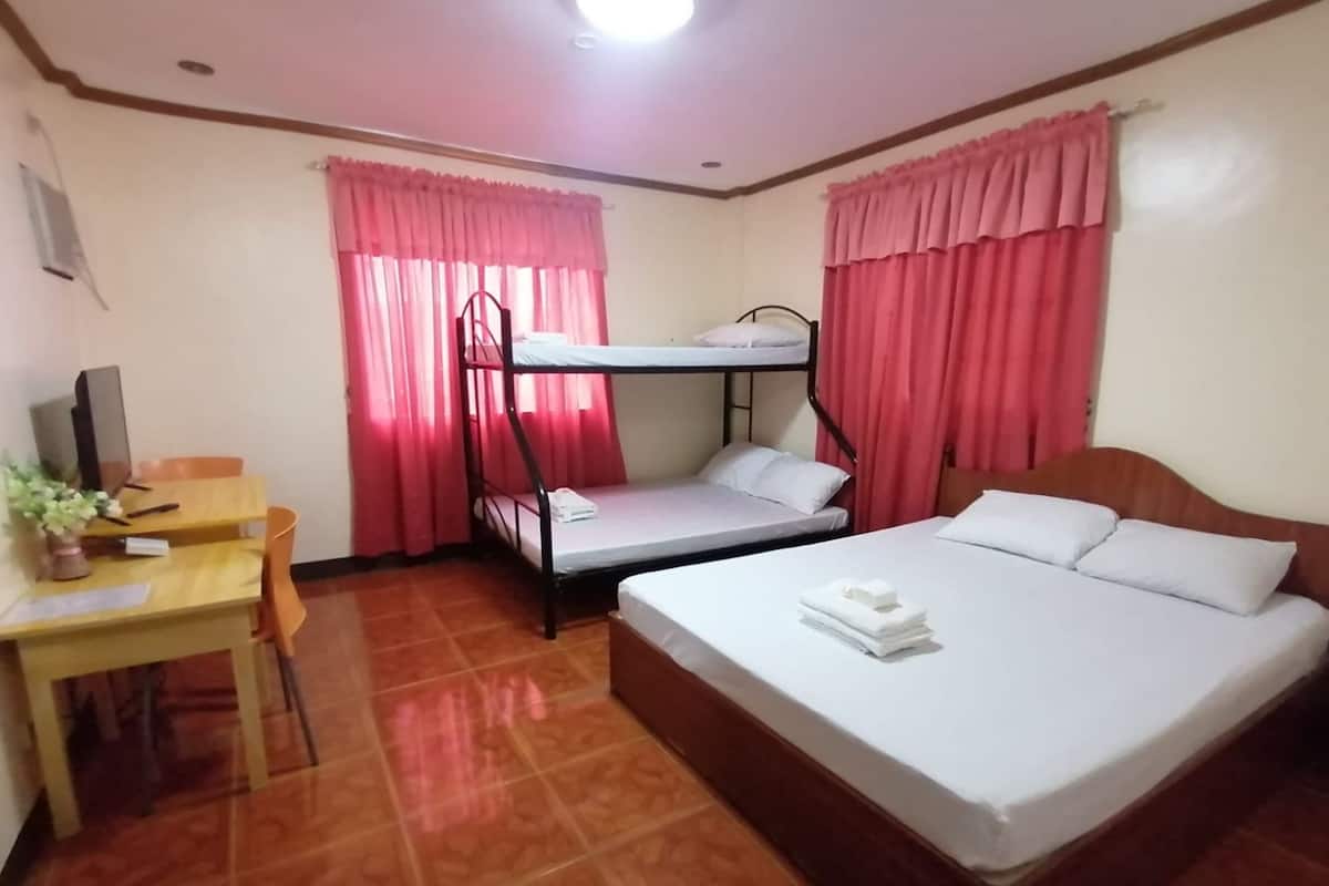 A room with a bunk bed, a single bed, a desk with a chair, and a television.