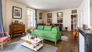 A living room with a green sofa, wooden furniture, and a dining area with chairs. - Picture Postcard, by Veeve (Paris)