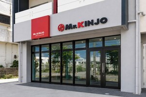 Egy „Mr. Kinjo” nevű üzlet, piros és fehér felirattal, nagy üvegportálokkal, és az ablakokon keresztül kilátással a környező területre.