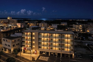 A multi-story hotel with a ground floor restaurant, a parking area, and a view of the sea. - Mr.KINJO LINK in Kugai Miyakojima (Miyakojima)