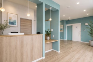 Zona de recepción con mostrador de madera, planta en maceta y un cuadro en la pared.