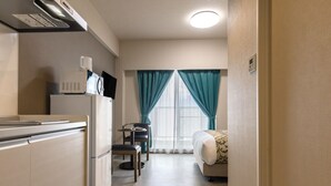 A compact hotel room with a kitchenette, a small dining table, a single bed, and a window with teal curtains. - Mr.KINJO LINK in Kugai Miyakojima (Miyakojima)