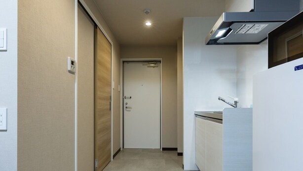 A narrow hallway with a door at the end, a kitchenette with a refrigerator and sink, and a ceiling light. - Mr.KINJO LINK in Kugai Miyakojima (Miyakojima)
