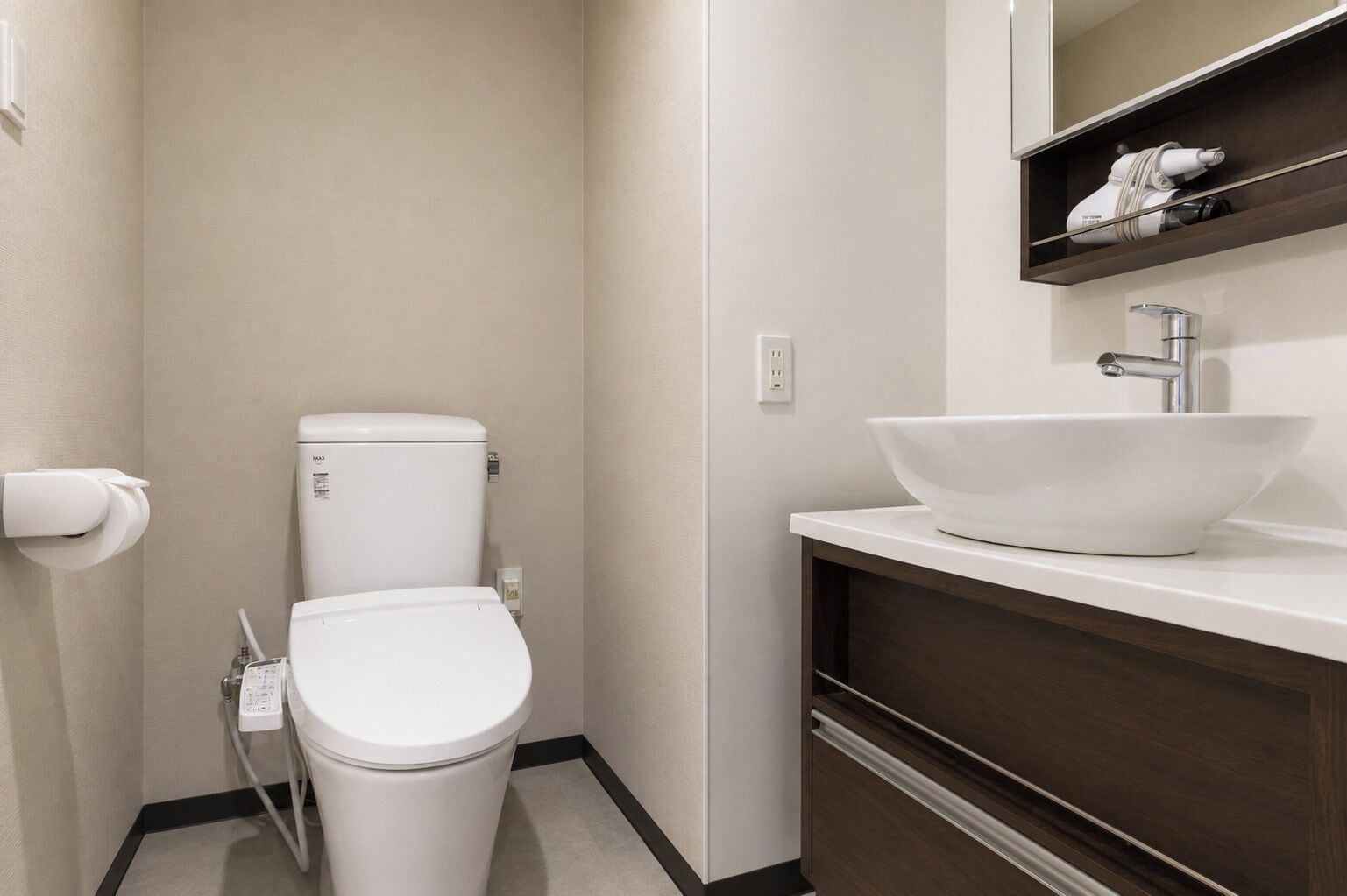 A modern bathroom with a toilet, a white sink, and a shelf above the sink.
