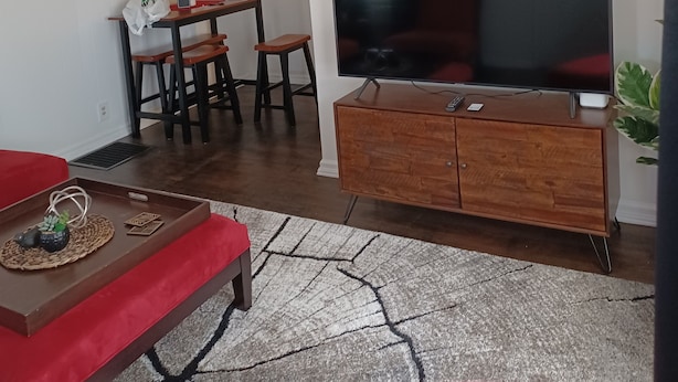 A modern living room with a large flat-screen TV, wooden furniture, and a patterned rug.