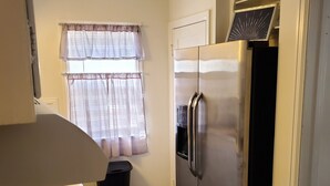 A kitchen with a gas stove, stainless steel refrigerator, and a window with sheer curtains.