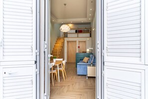 An open door leading to a dining area with a table and chairs, a staircase, and a blue sofa in the background.