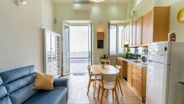 A compact living space with a sofa, dining table, chairs, kitchen area, and a balcony. - GuestHost - Cozy 50 sqm apartment, able to accommodate up to 3 people, located on the ground floor of a building facing the beach. The property is located in Giardini Naxos, a wonderful seaside area 1.8 km from the pretty village of Schisò and just 2 km (Giardini Naxos)