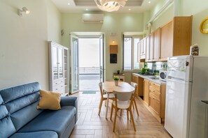 Ein kompakter Wohnbereich mit Sofa, Esstisch, Stühlen, Küchenzeile und einem Balkon.
