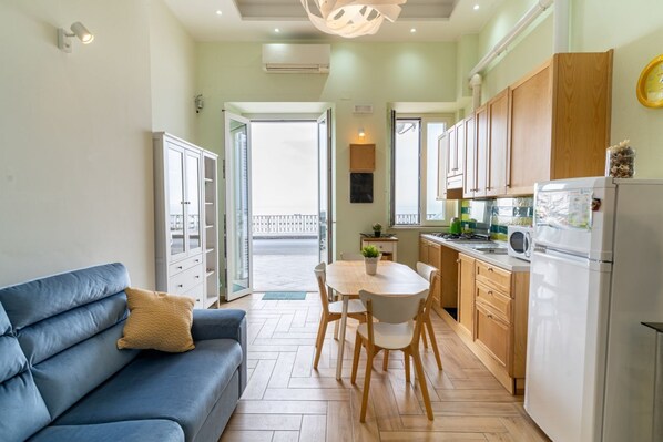 A compact living space with a sofa, dining table, chairs, kitchen area, and a balcony.