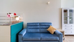 A blue sofa with a cushion, a cabinet with glass doors, and a wall-mounted lamp. - GuestHost - Cozy 50 sqm apartment, able to accommodate up to 3 people, located on the ground floor of a building facing the beach. The property is located in Giardini Naxos, a wonderful seaside area 1.8 km from the pretty village of Schisò and just 2 km (Giardini Naxos)
