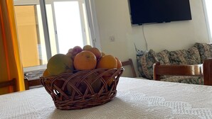 A dining area with a table set for two, a wicker fruit basket, a television mounted on the wall, and a window with curtains. - Grand Duplexe Mer et Piscine in Tangier (طنجة)