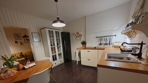 A modern kitchen with wooden countertops, a dining area with a wooden table and white chairs, a white cabinet with glass doors, and a hanging light fixture. - Stunning 2-bed House in Jezera With Sea Views (Tisno)