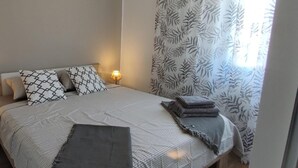 A bedroom with a bed, pillows, a bedside lamp, and a window with patterned curtains. - Stunning 2-bed House in Jezera With Sea Views (Tisno)
