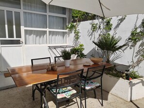 An outdoor patio with a wooden table and chairs, surrounded by potted plants and a white wall. - Stunning 2-bed House in Jezera With Sea Views (Tisno)
