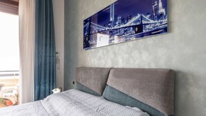 Ein Schlafzimmer mit Bett, Kopfstütze, einem Fenster mit Vorhängen und einem Stadtbild an der Wand.