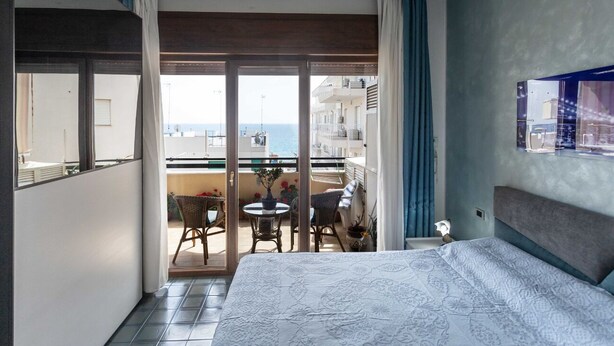 Ein Hotelzimmer mit Bett, einem Balkon mit Tisch und Stühlen sowie Blick auf das Meer.