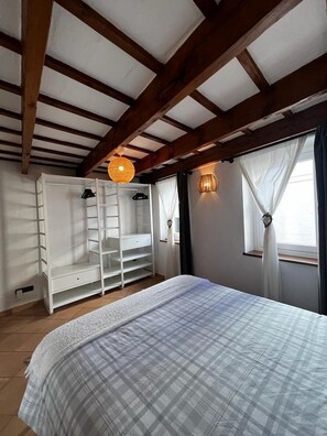 Een slaapkamer met een bed, een kledingkast, een hanglamp en een raam met gordijnen.