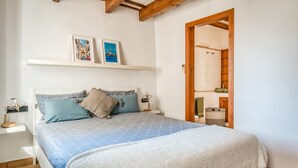 Ein Schlafzimmer mit einem Bett, einem Nachttisch, einem Regal mit Bildern und einer Holztür zu einem Badezimmer.