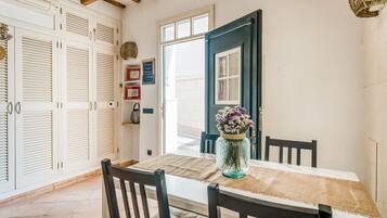 A dining area with a table set for two, a vase with flowers, and a view of the outside.