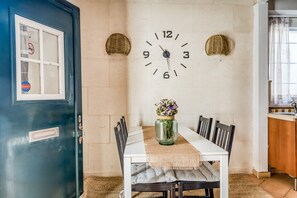 Een eethoek met een witte tafel, zwarte stoelen, een klok aan de muur en een vaas met bloemen.
