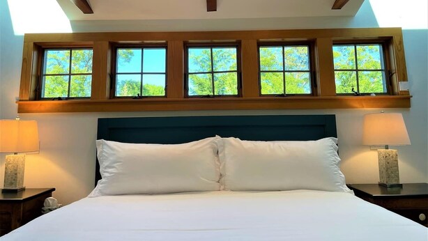 A bedroom with a large bed, a wooden headboard, and a skylight above. - Private beach, hot tub, and dog friendly – The Keeper! (Brewster)