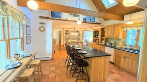 A spacious kitchen with a large island, wooden cabinets, and a dining area with a long table and chairs. - Private beach, hot tub, and dog friendly – The Keeper! (Brewster)