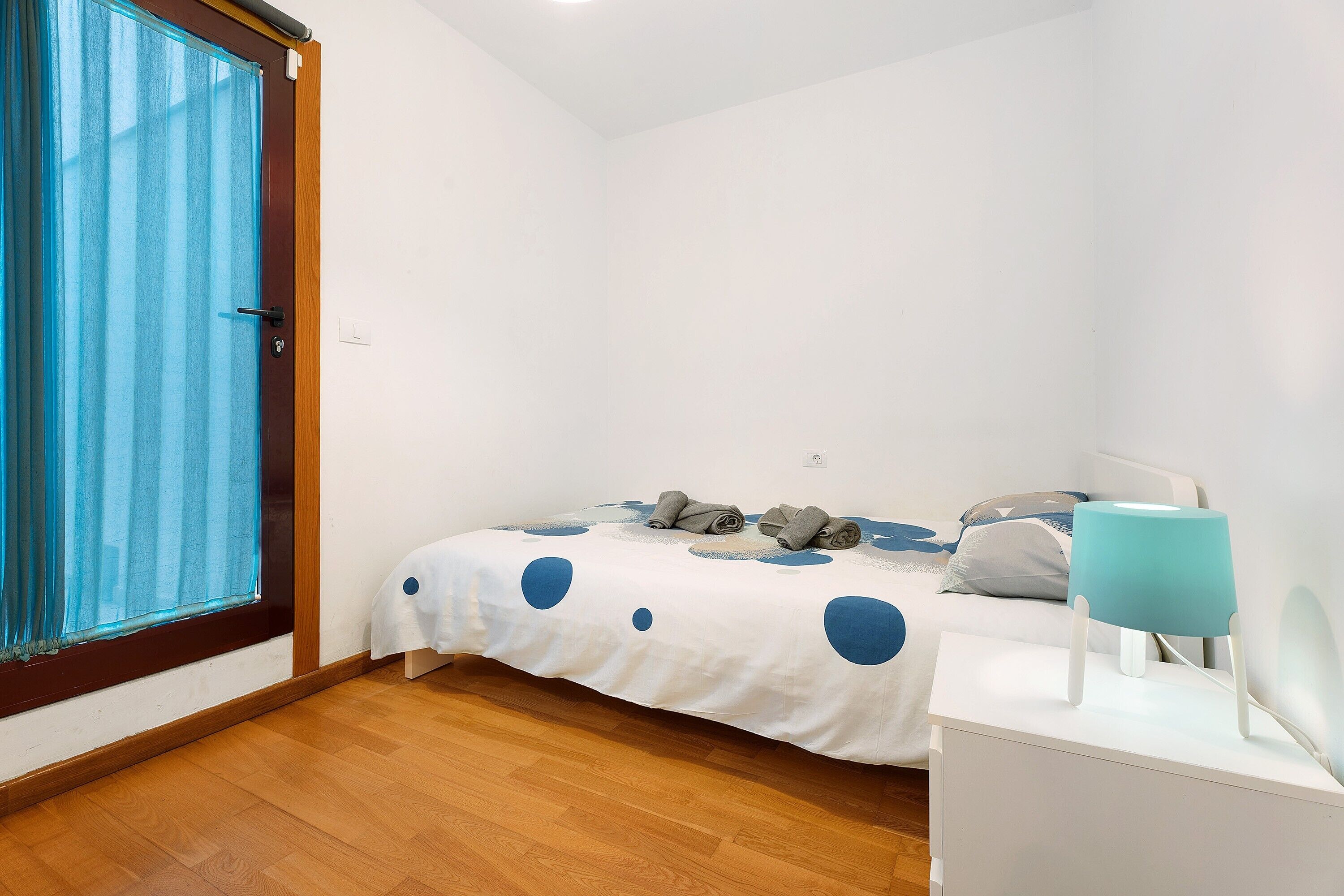Un dormitorio con una cama, una mesita de noche, una lámpara y una ventana con cortinas.