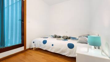 Un dormitorio con una cama, una mesita de noche, una lámpara y una ventana con cortinas.